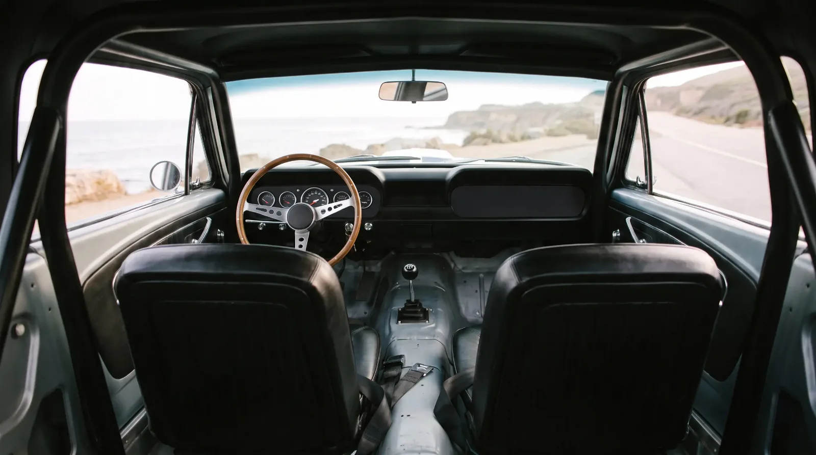 1965 Shelby GT350R stripped cockpit with roll bar and bare floor, parked on a coastal road