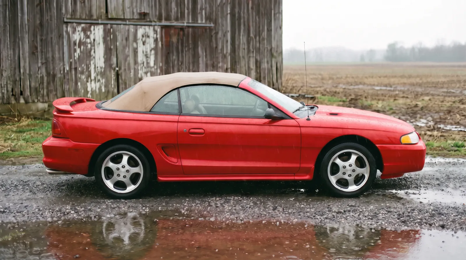 1994 Ford Mustang Cobra convertible in Rio Red, parked by a barn in the rain