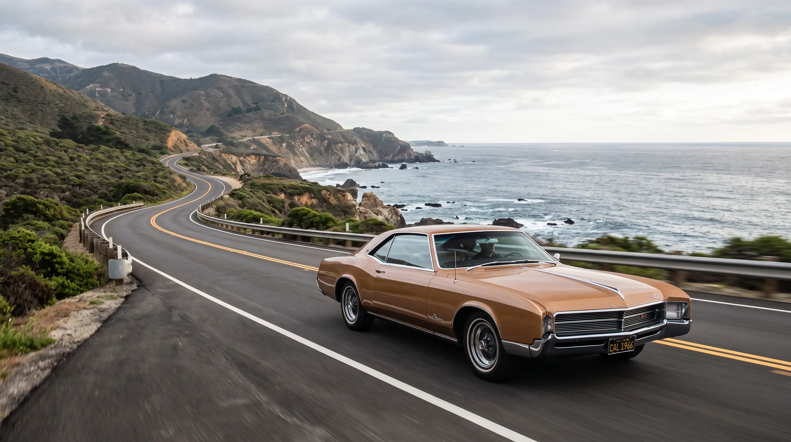 Bronze 1966 Buick Riviera cruising a coastal road in soft daylight