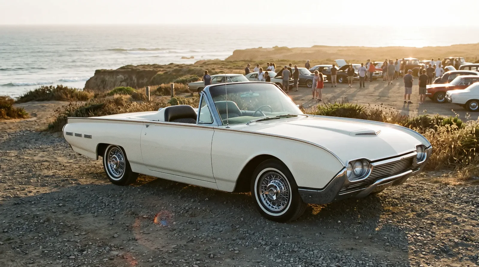 A coastal classic car meet at golden hour with a 1962 Ford Thunderbird Sports Roadster