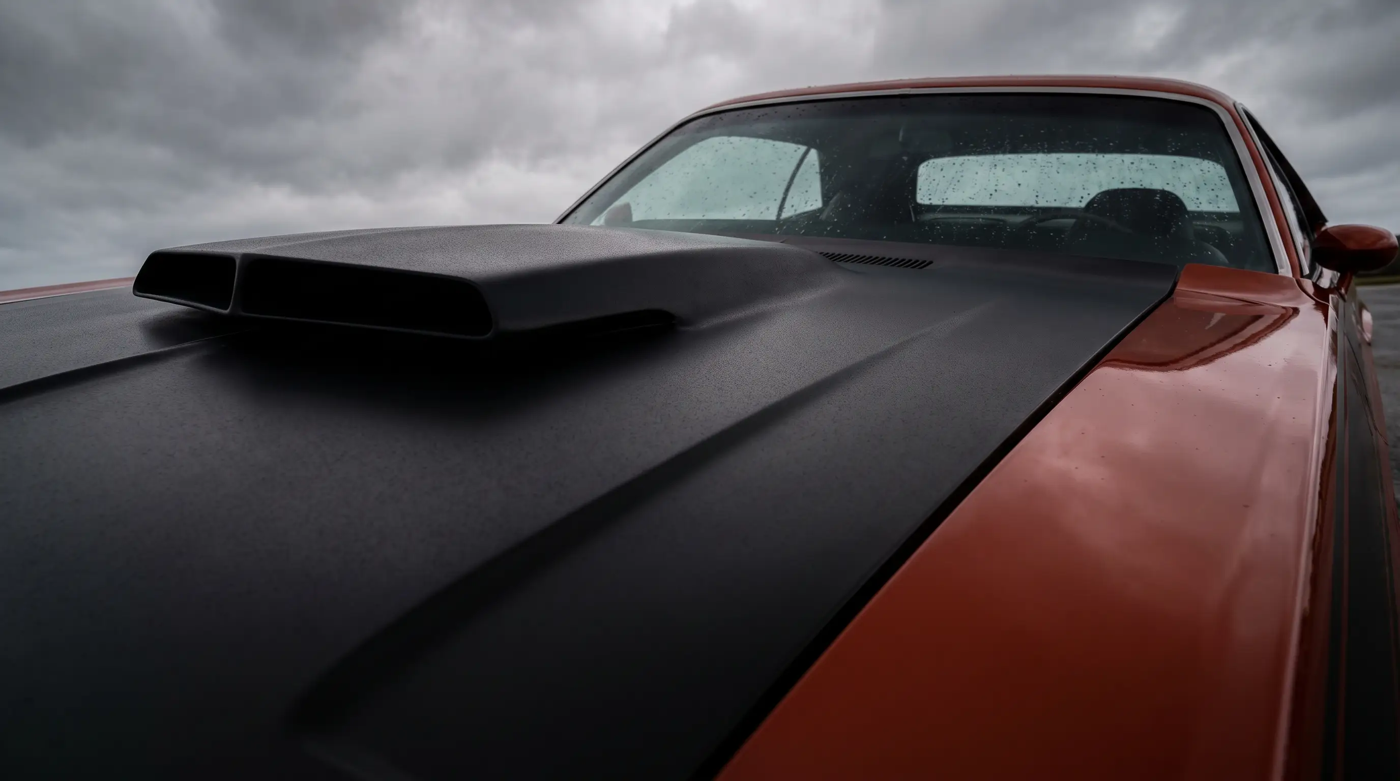 Close view of the matte black fiberglass hood scoop on a Challenger T/A under overcast light