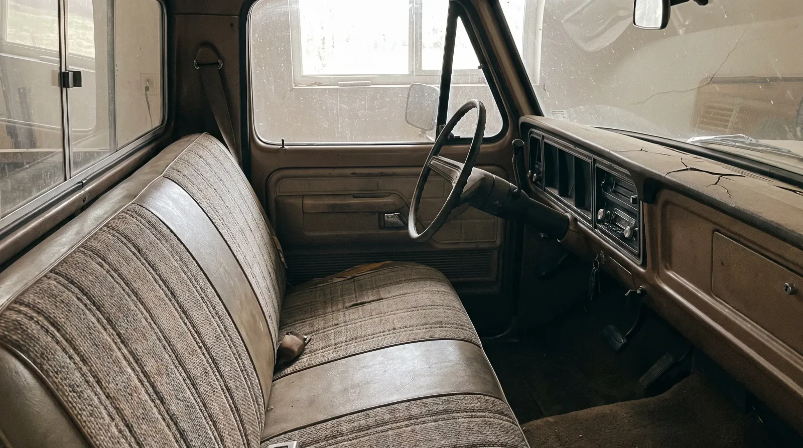 Worn but intact interior of a 1970s pickup with a faded bench seat and cracked dash, typical of a driver-quality car