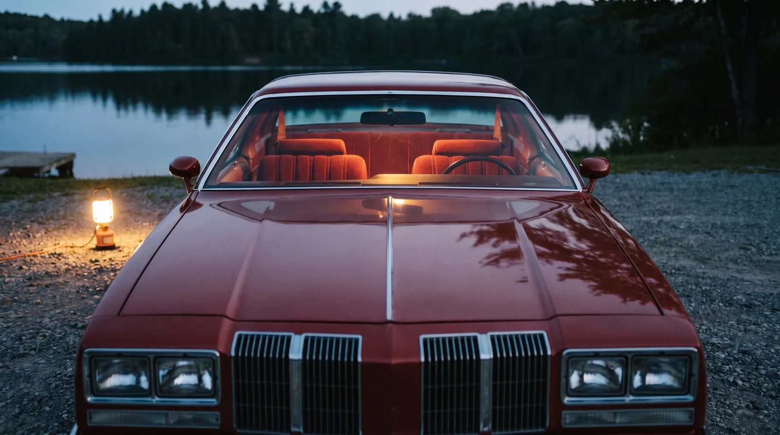 1976 Oldsmobile Cutlass Supreme — cabin seen through the windshield at a lakeside lot
