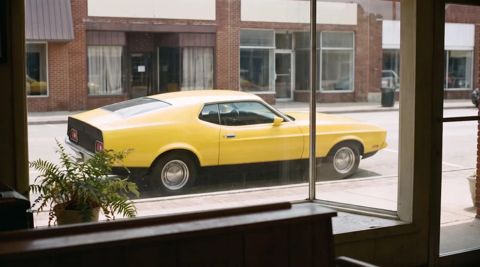 1971 Ford Mustang Mach 1 in Grabber Yellow, seen through a shop window on a small-town main street