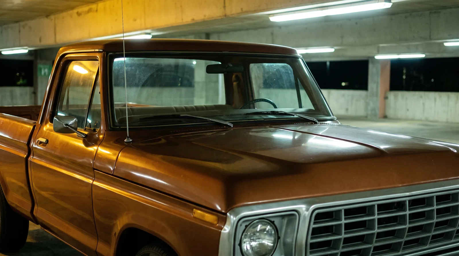 1977 Ford F-100 dentside pickup — through the windshield in a night parking garage