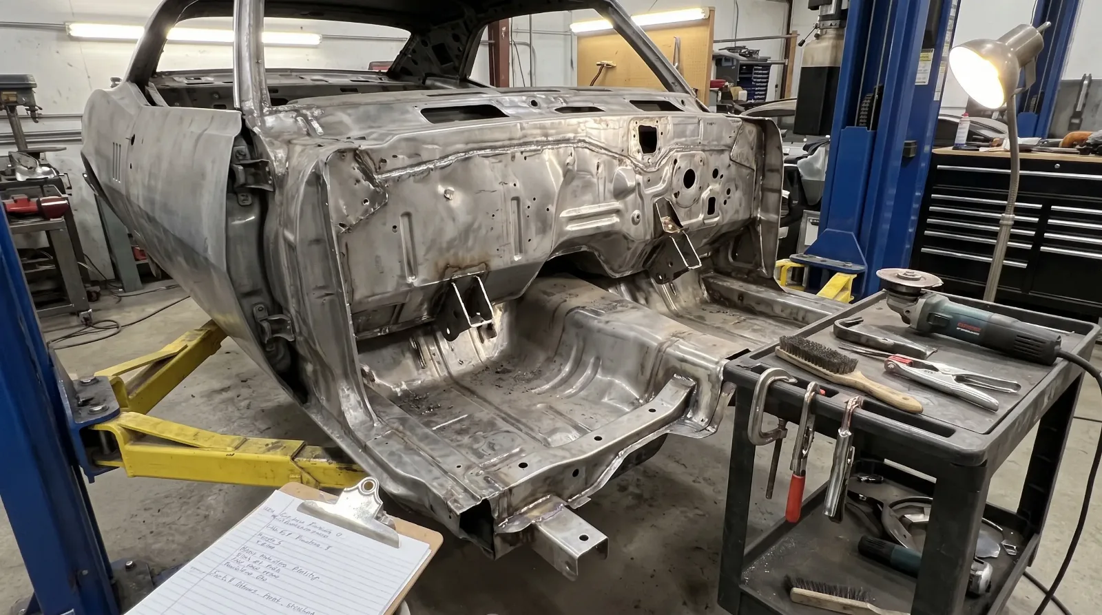 Bare 1967 Pontiac Firebird unibody shell on a restoration lift showing shared F-body floor pan and firewall stampings