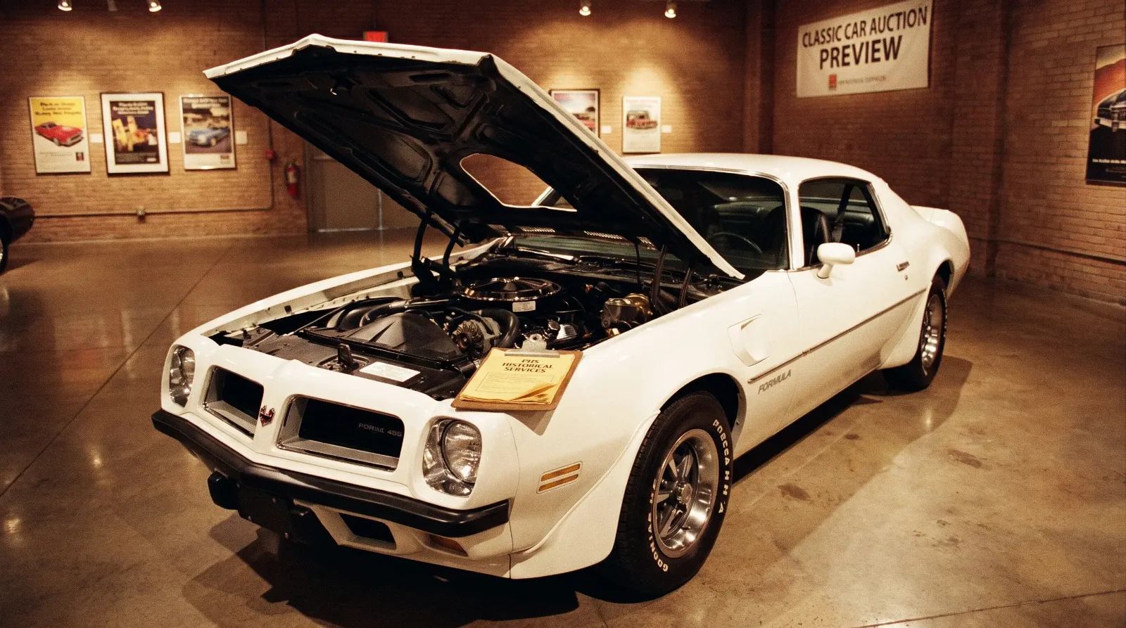 Pristine 1974 Pontiac Firebird Formula 455 with hood open in a gallery setting, documentation resting on the fender