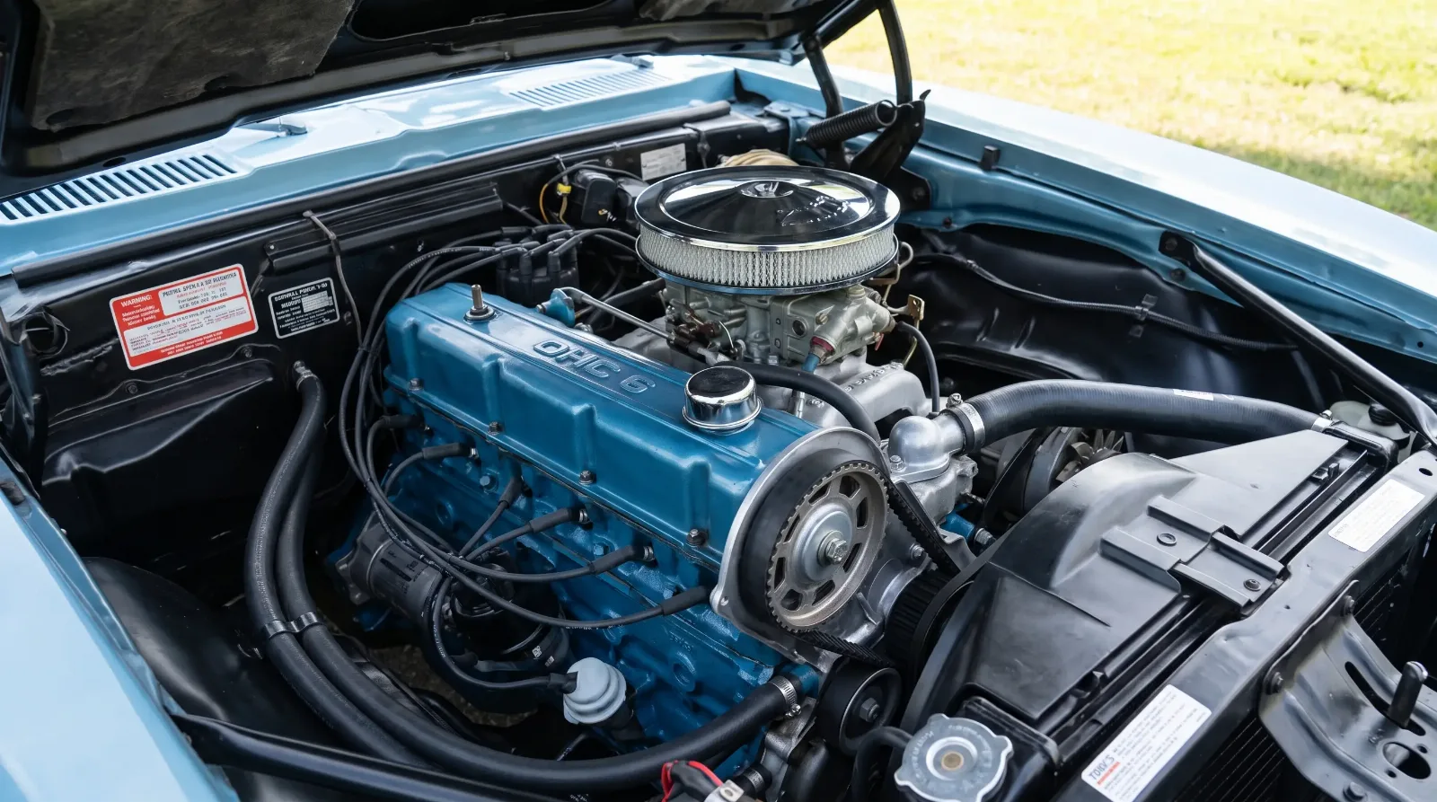 Engine bay detail of a 1967 Pontiac Firebird OHC Sprint Six showing the toothed timing belt and Rochester four barrel carburetor