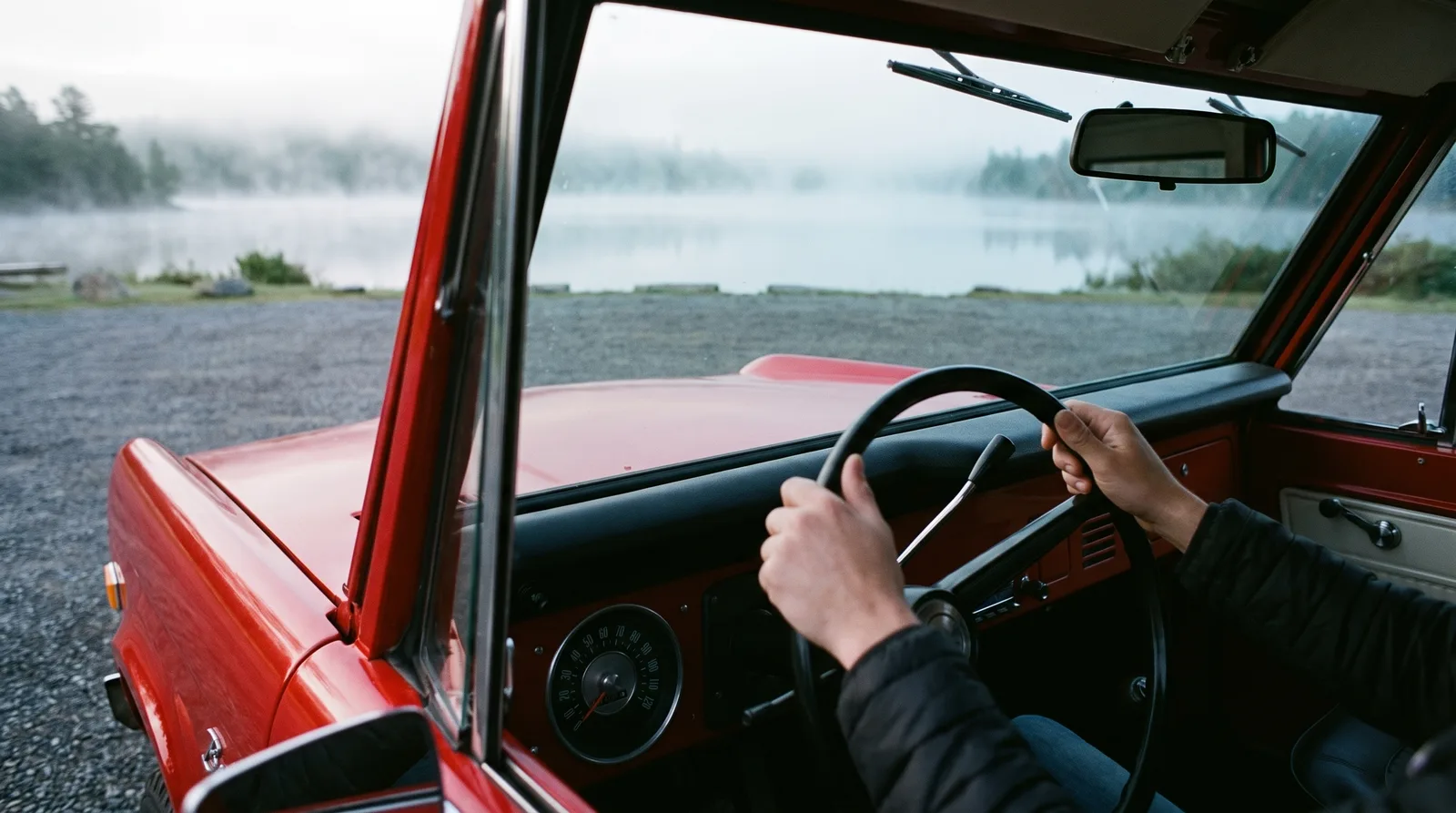 1969 Ford Bronco, red hood seen from the cab by a misty lake