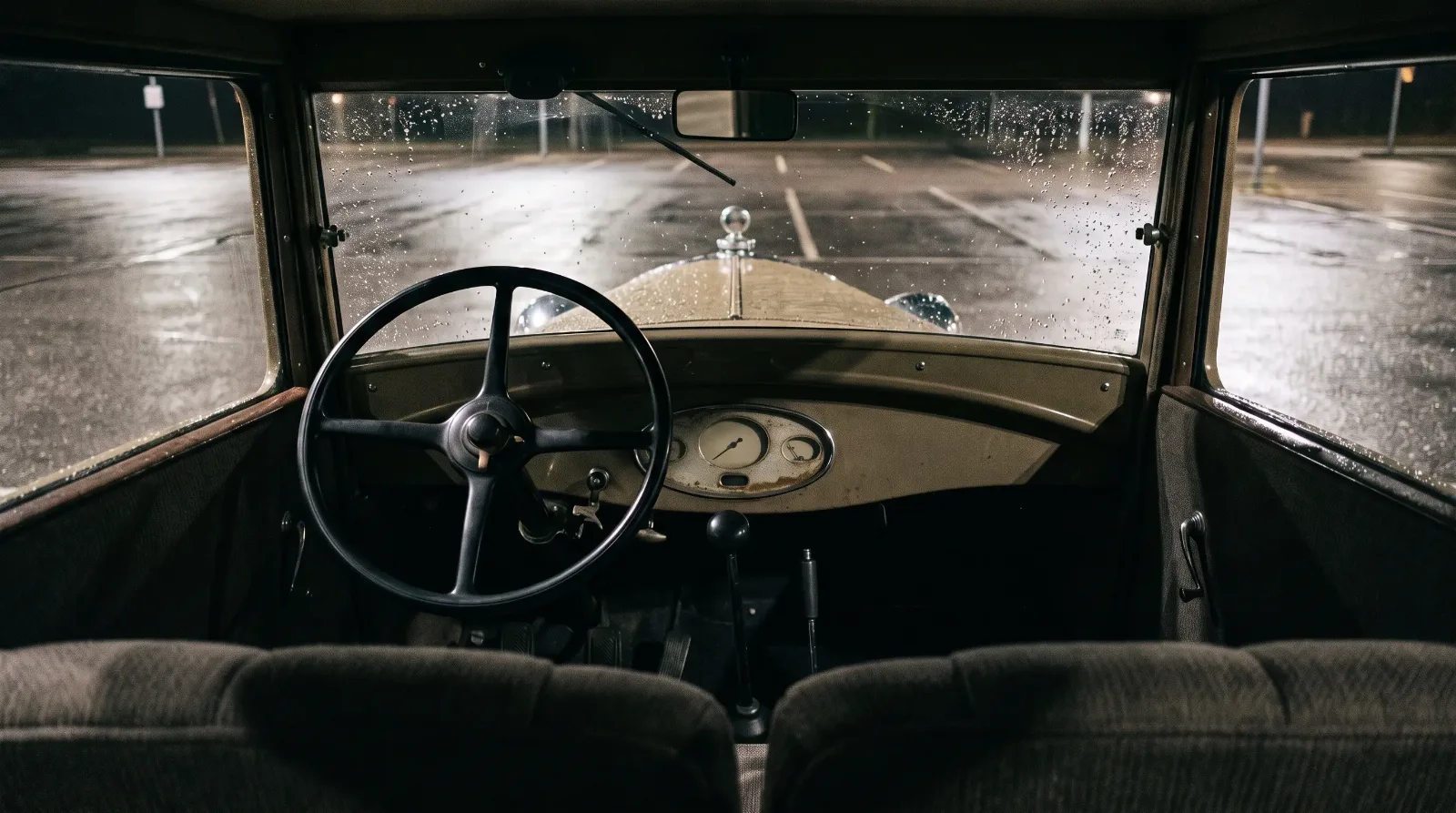 1928 Ford Model A Tudor cockpit with floor gearshift and three pedals, seen through a rainy windshield