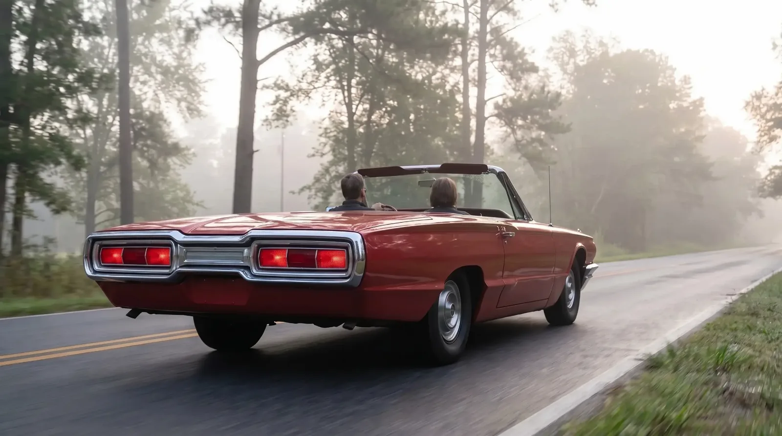 Red 1964 Thunderbird convertible with two people driving down a misty country road