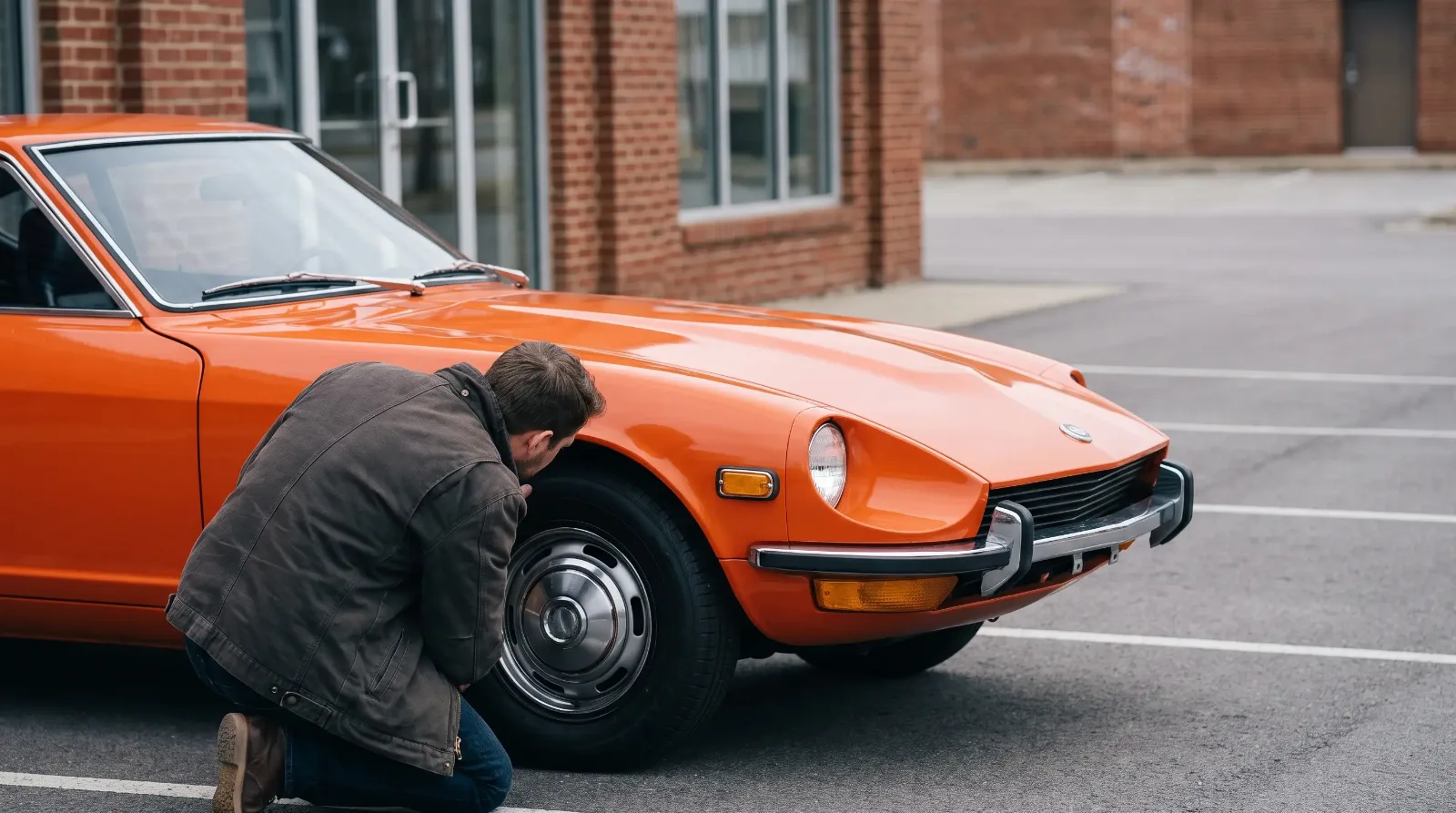 Owner kneeling to check the tire and fender of an orange 1972 Datsun 240Z at pickup