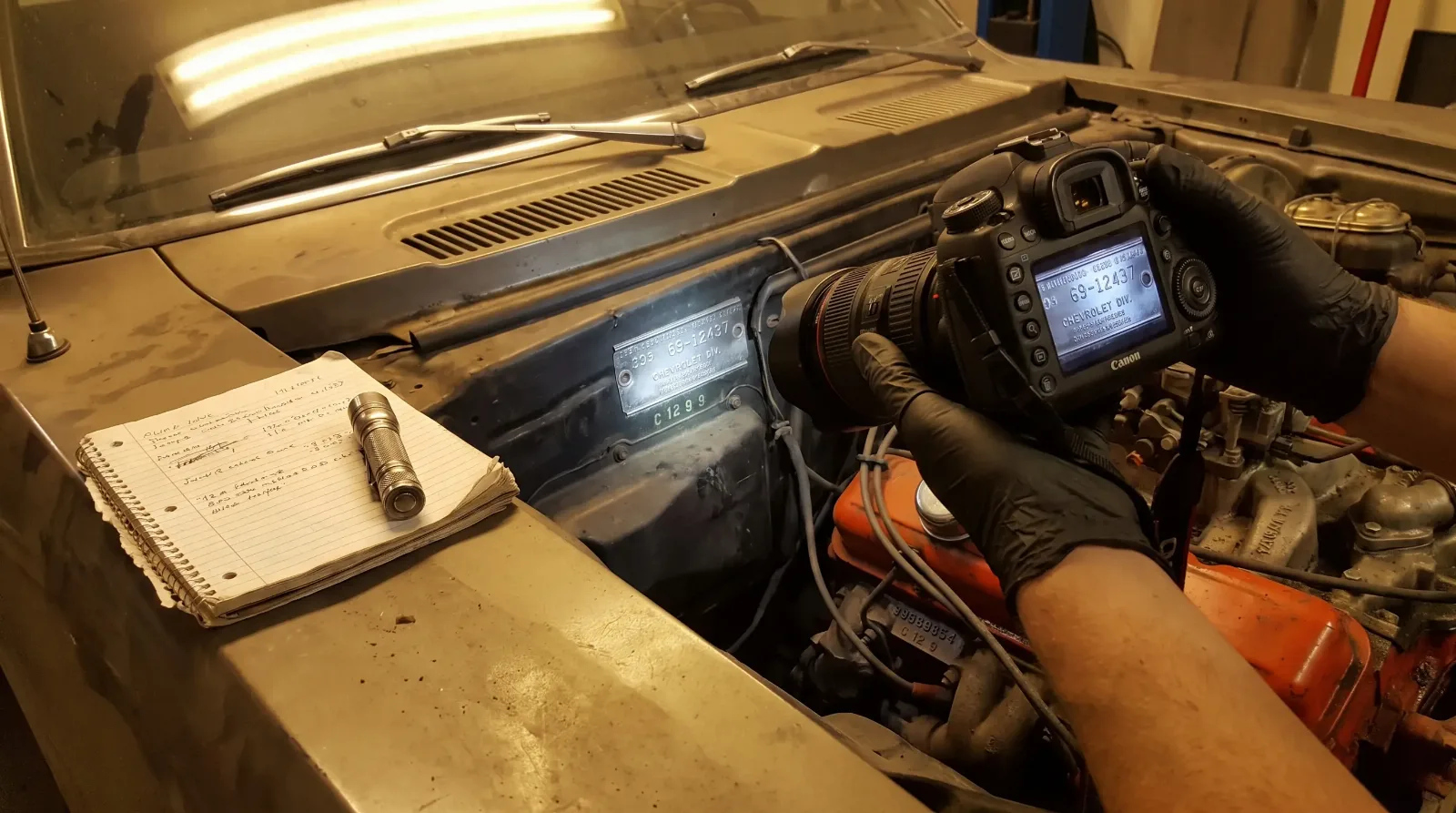 Hands photographing the cowl tag and firewall of a 1969 Chevrolet Camaro during documentation