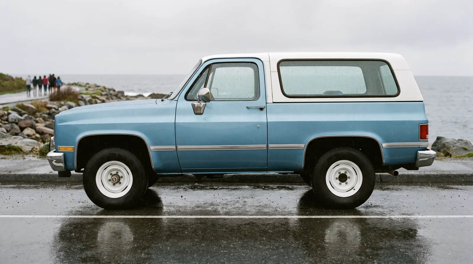 1980s Chevrolet K5 Blazer, light blue squarebody on a coastal road in rain