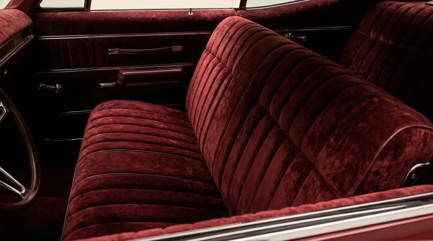 Close cabin view of a lowrider tuck-and-roll interior with deep burgundy crushed-velvet pleated bench seat and door panels and chrome trim