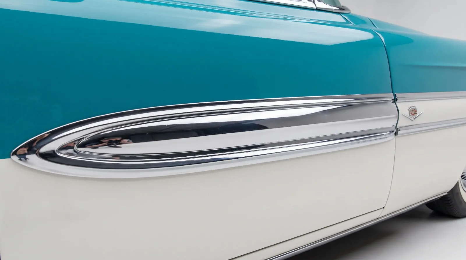 Side-panel detail of a 1956 Cadillac showing a turquoise-and-white two-tone paint split divided by a chrome spear molding