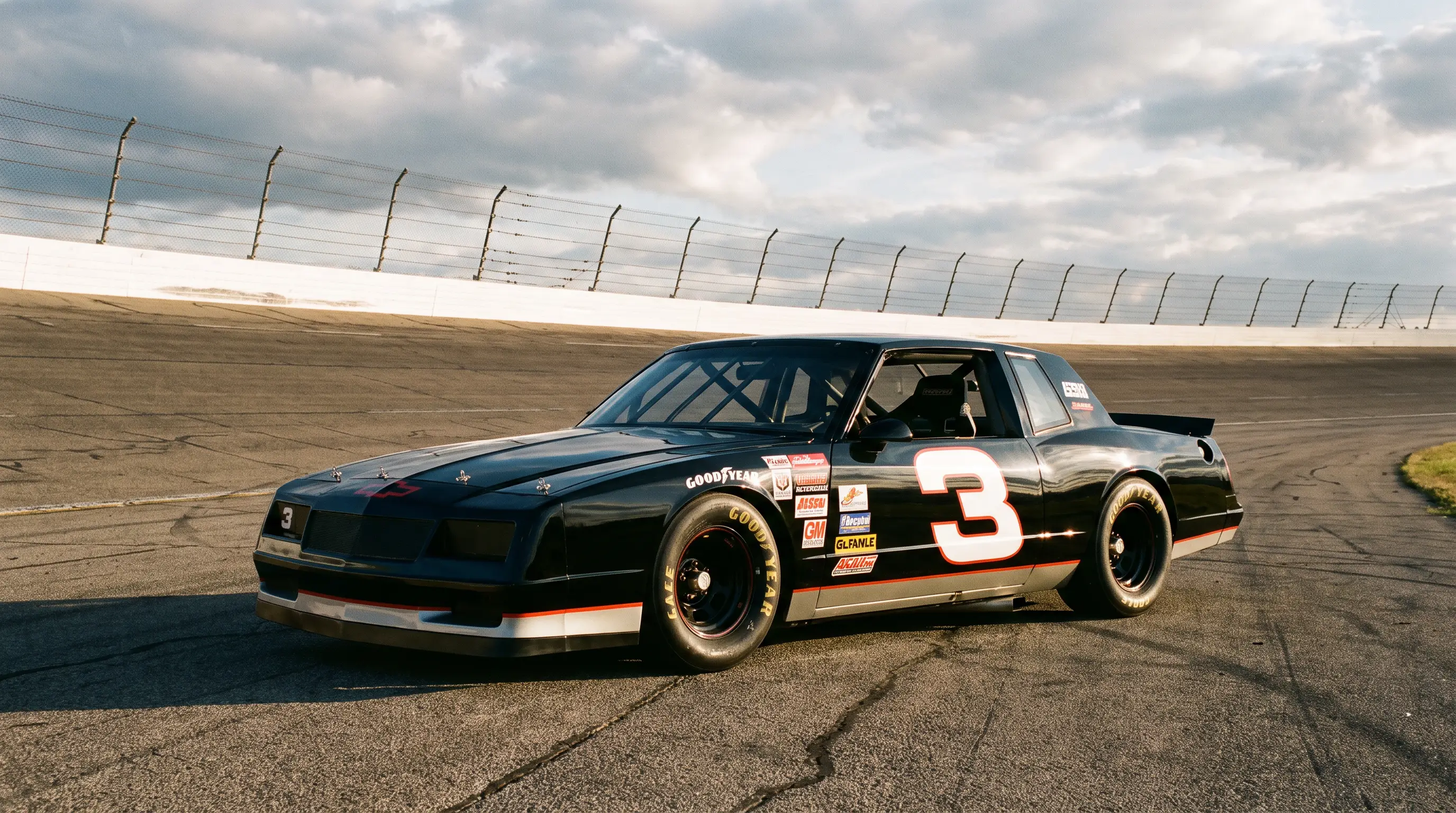 Black 1987 NASCAR Monte Carlo SS stock car parked on a sunlit speedway apron