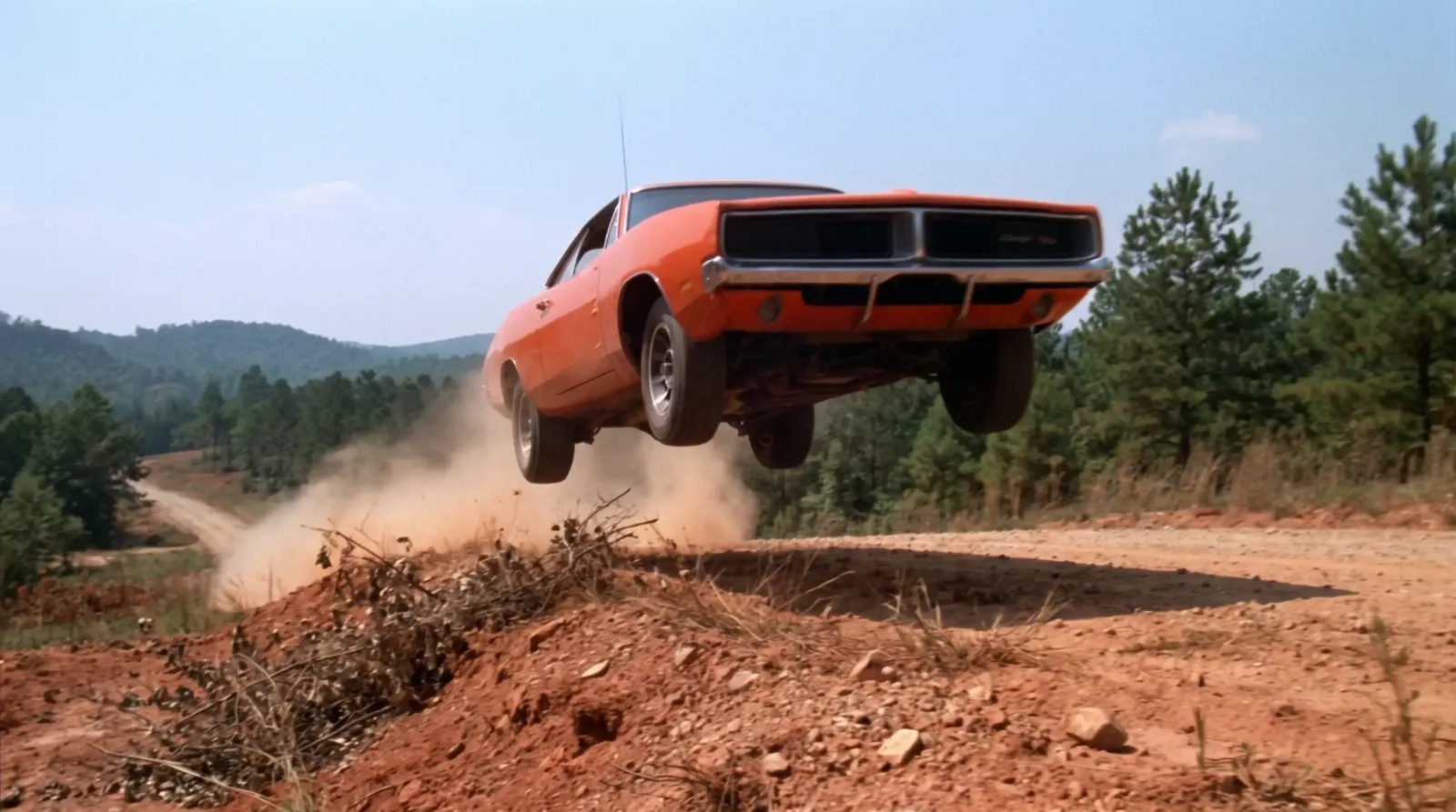 Bright orange late-1960s muscle coupe airborne over a dirt embankment on a rural Southern road