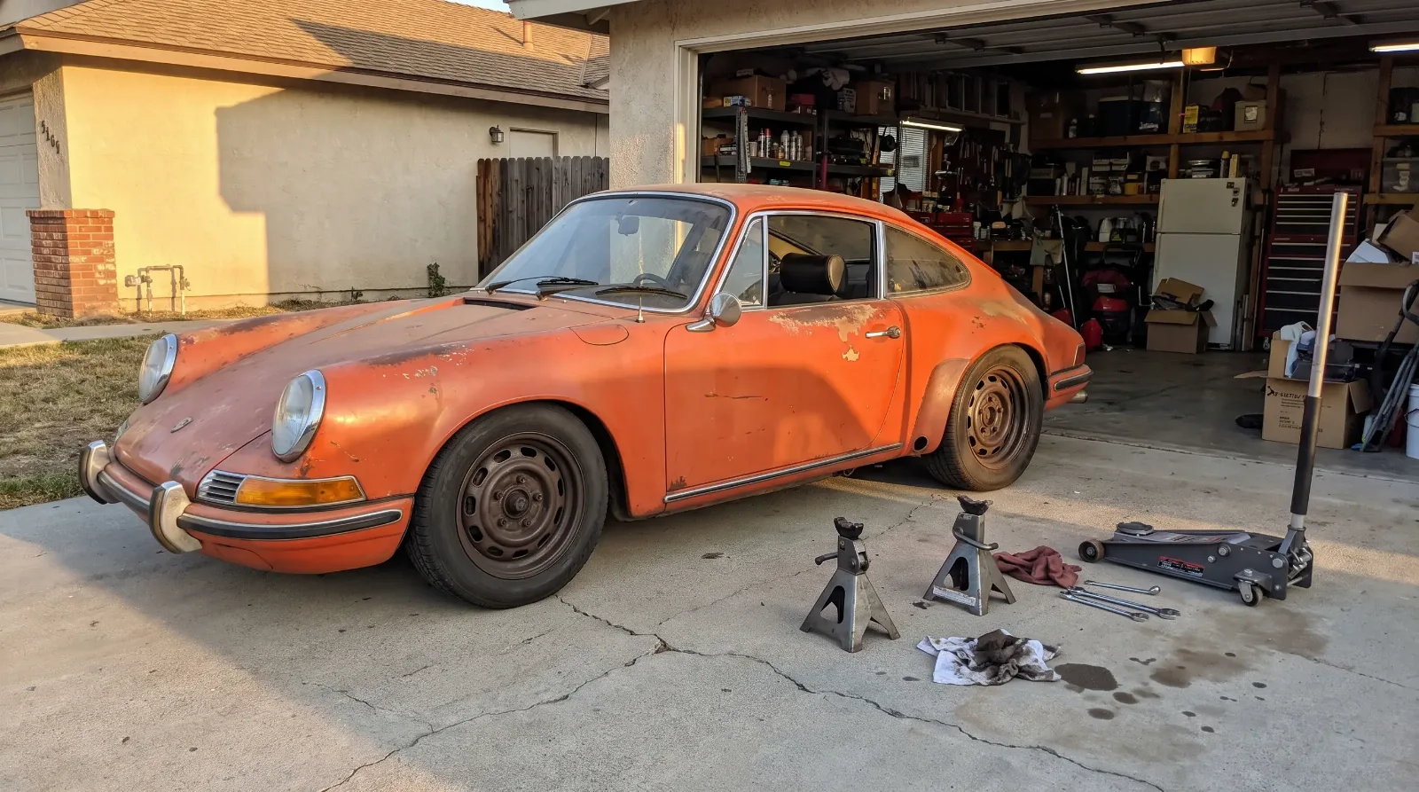 Lowered outlaw Porsche 912 with flared rear fenders parked in a home garage driveway at golden hour