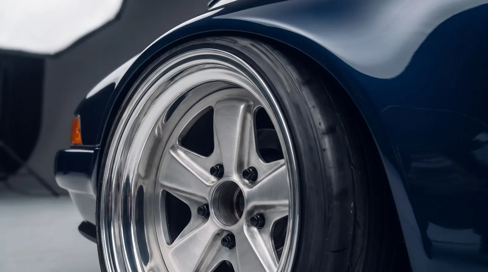 Macro detail of a polished five-spoke Fuchs alloy wheel on a widened air-cooled Porsche 911 rear fender