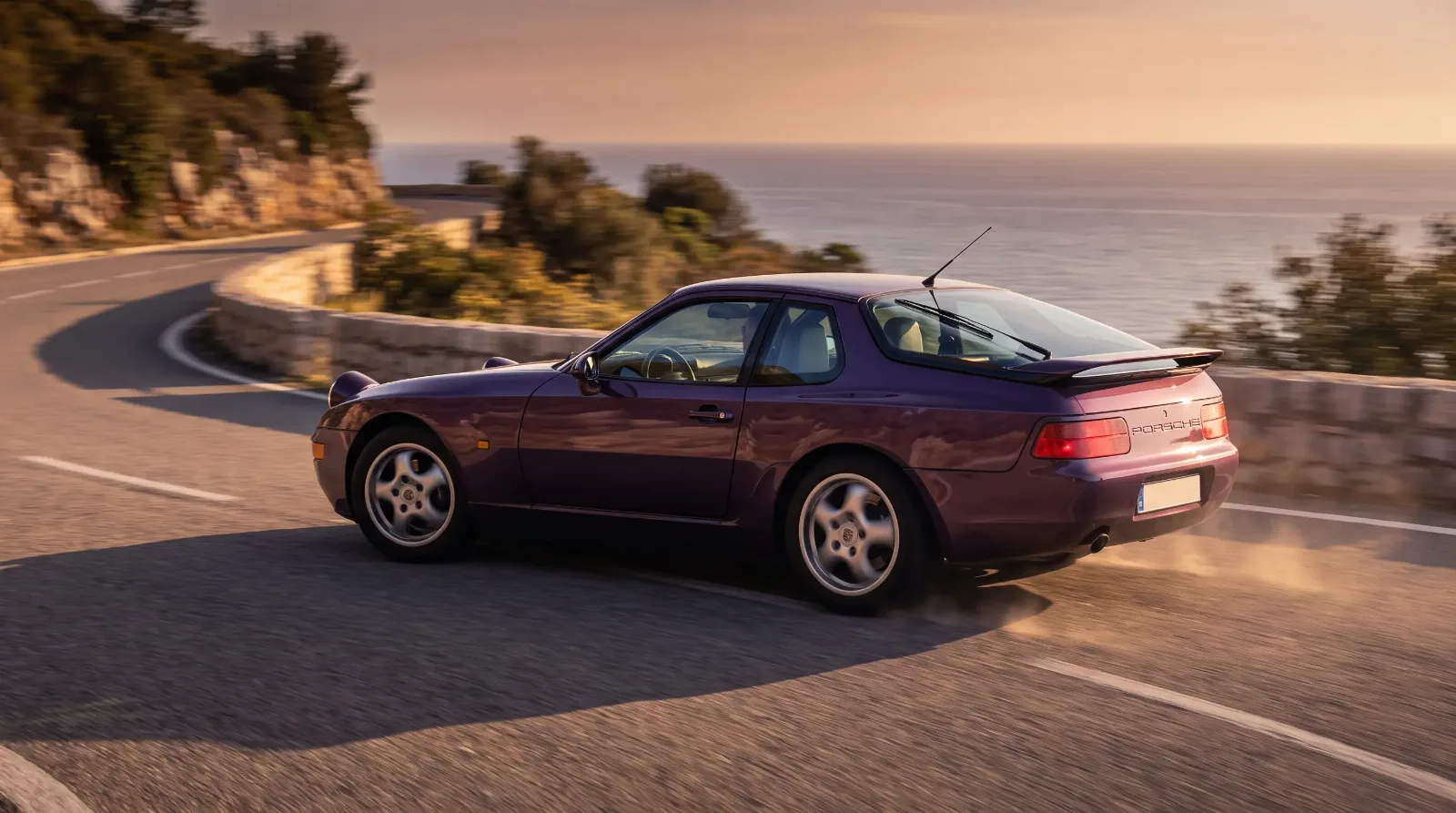 1993 Porsche 968 Coupe in purple driving a coastal European road at sunset