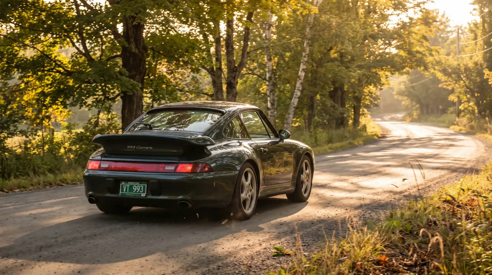 Dark green 1997 Porsche 993 Carrera driving a tree-lined Vermont back road at golden hour