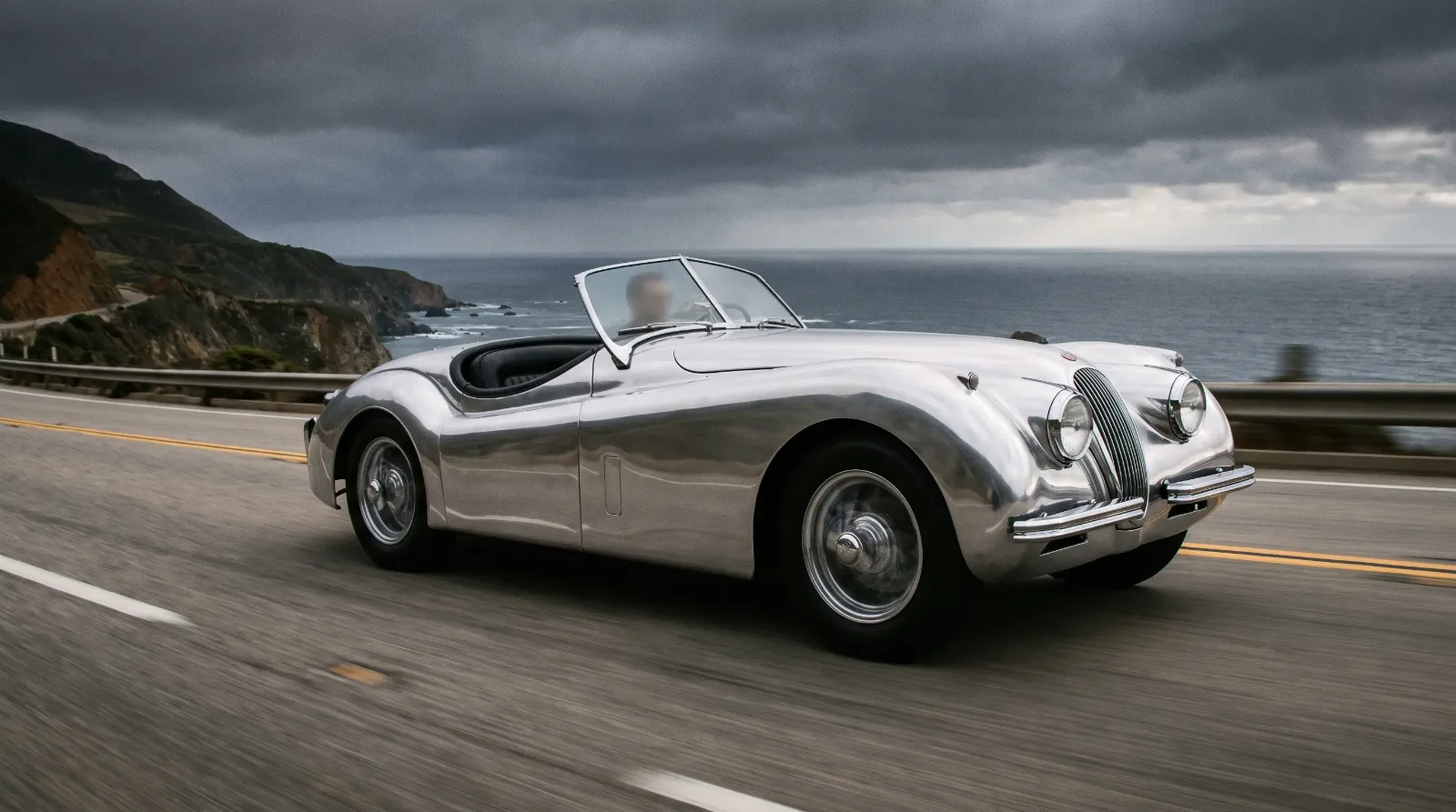 Jaguar XK120 roadster racing along coastal road