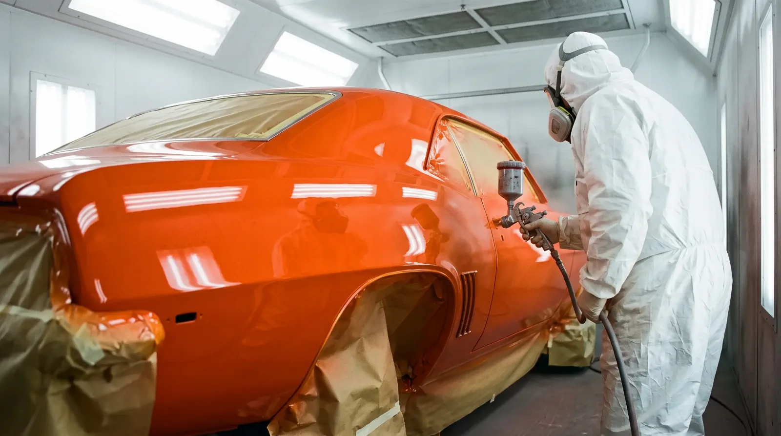 Painter spraying the rear quarter of a 1969 Chevrolet Camaro in a paint booth