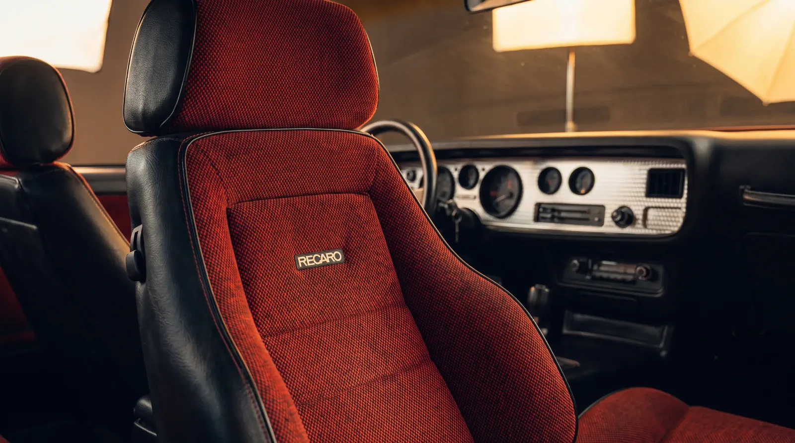 Close-up studio detail of a red and black Recaro sport bucket seat inside a 1982 Pontiac Trans Am