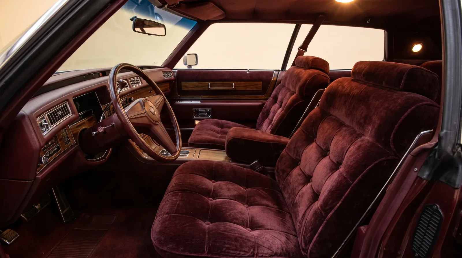 Interior of a 1975 Cadillac Fleetwood with button-tufted maroon crushed velour seats and simulated woodgrain dash, the classic land yacht cabin