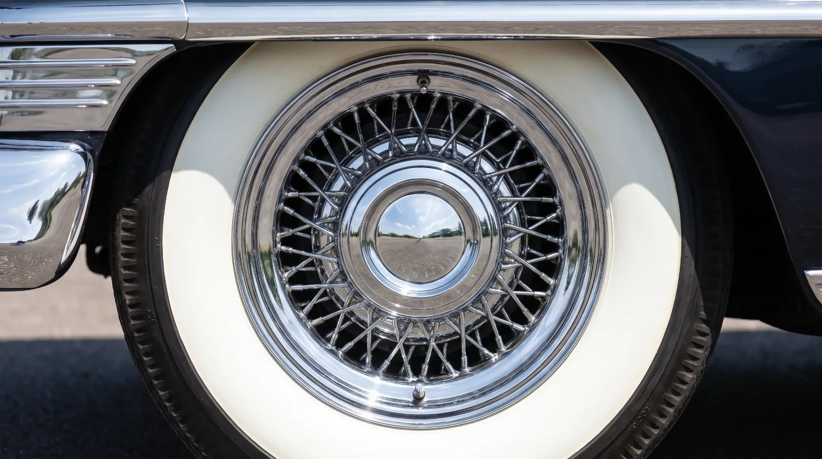 Wide whitewall tire and chrome wire wheel cover detail
